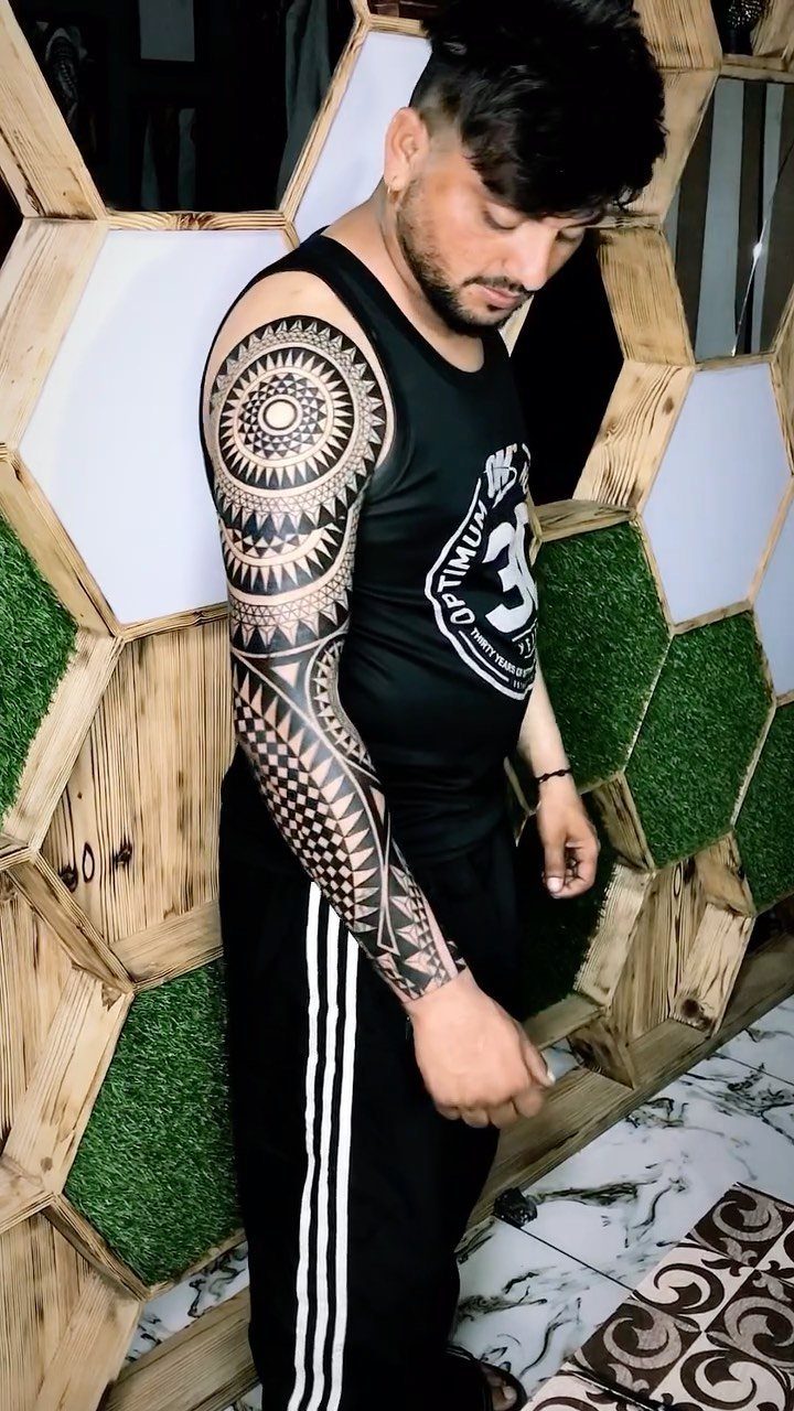 Man with a full geometric tattoo sleeve on his right arm posing indoors.