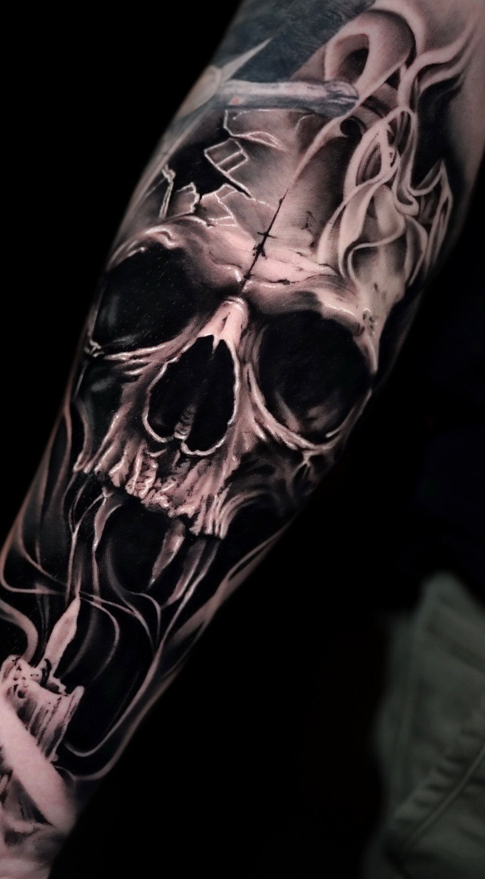 Detailed black and grey skull tattoo with smoke swirls on a man's arm.