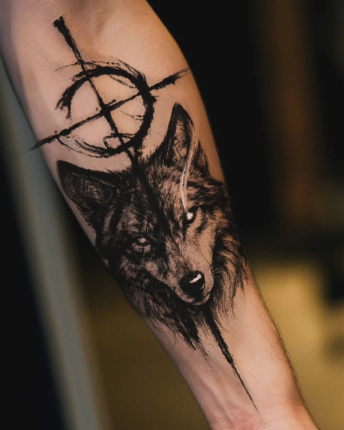 Wolf head tattoo with abstract circular symbol on a man's forearm