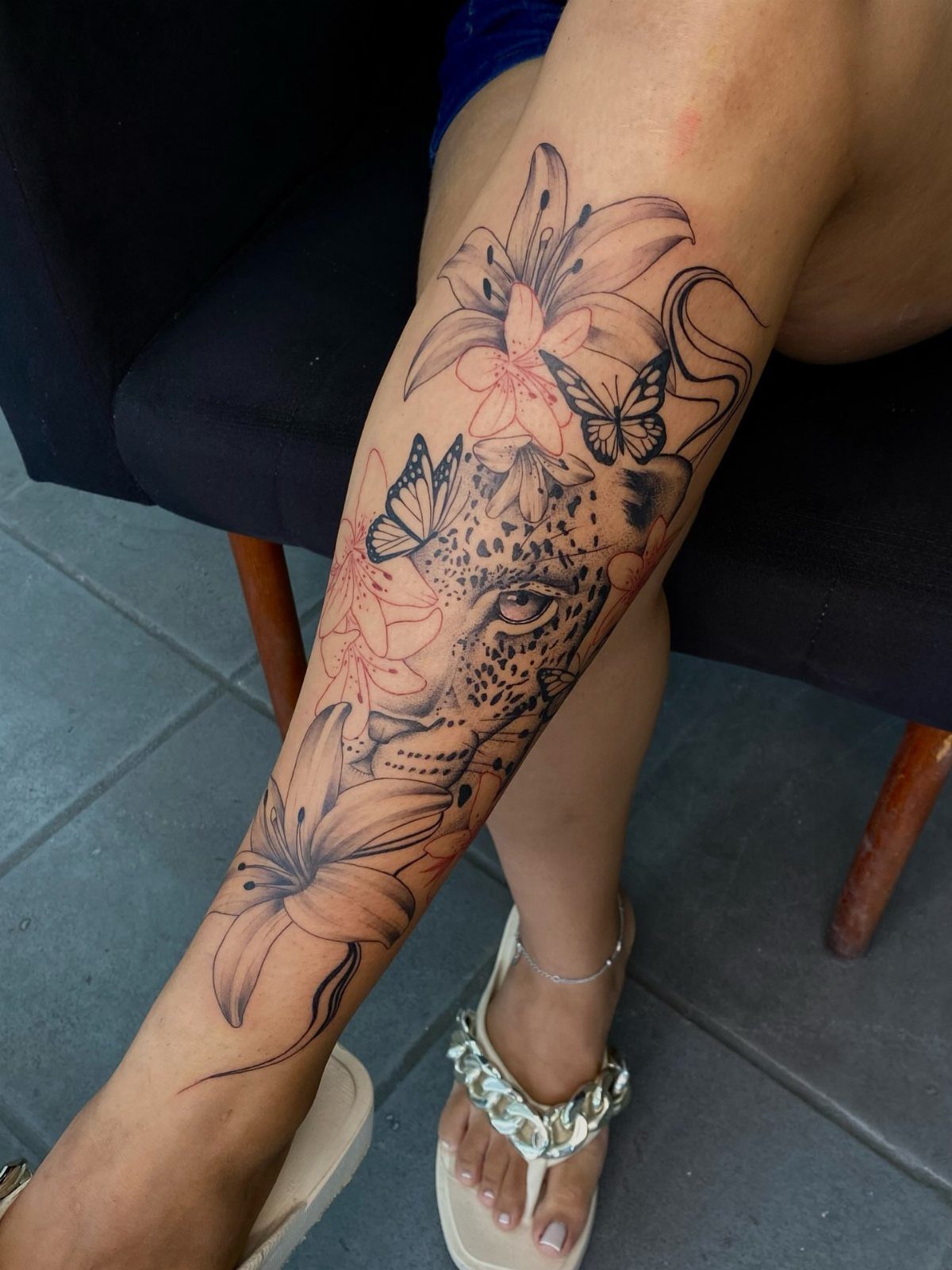 Leopard face tattoo with lilies and butterflies on a woman's leg