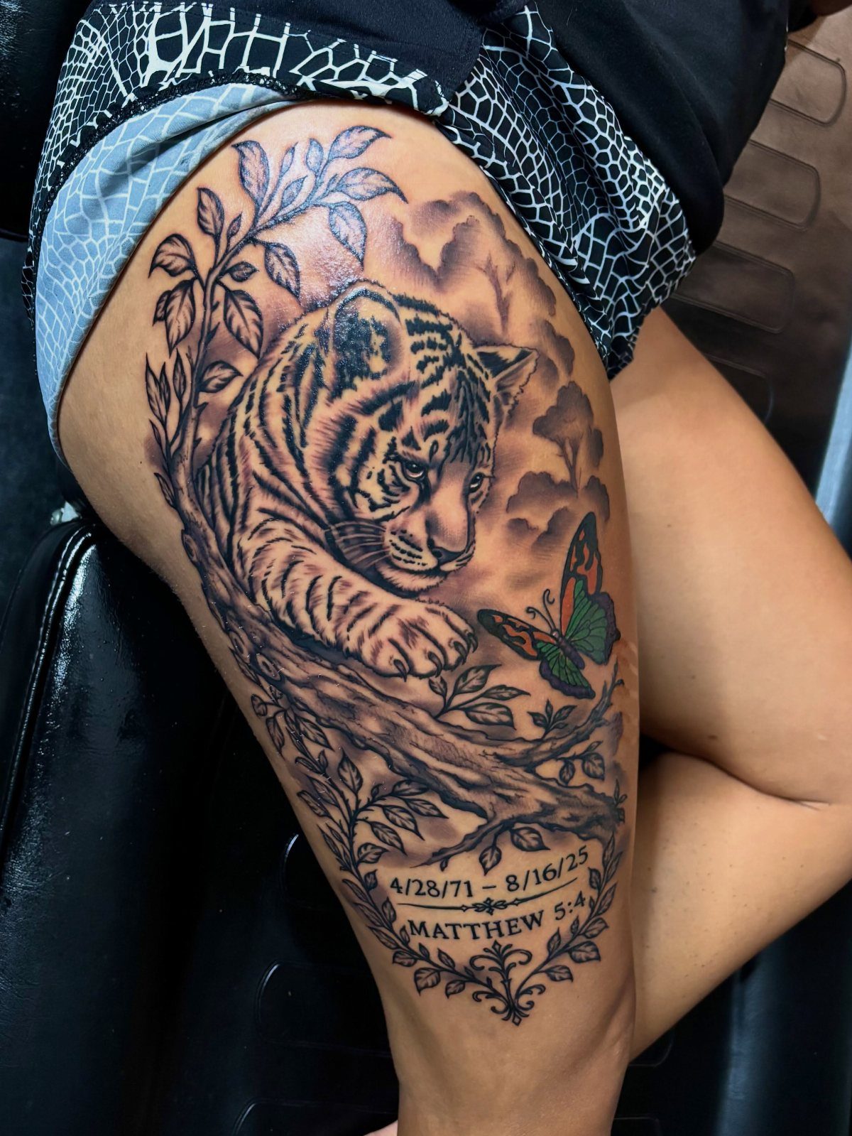 Tiger cub tattoo on a thigh with a butterfly and memorial text.