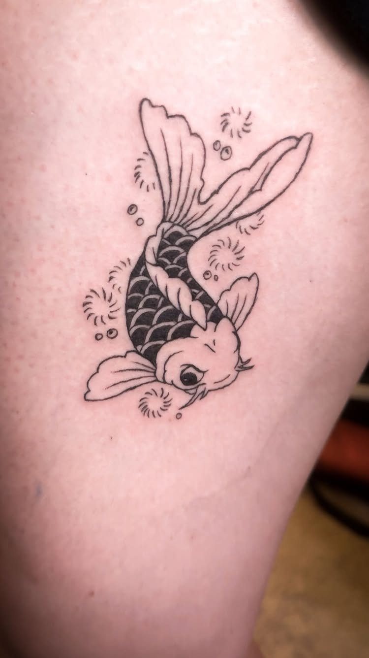 Koi fish tattoo with black ink and flowing fins on a person's thigh