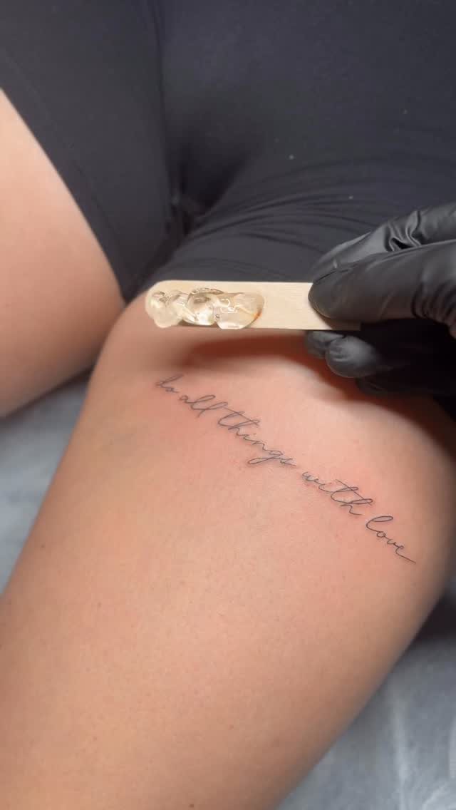 Cursive lettering tattoo on a woman's thigh reading do all things with love