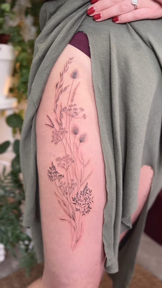 Wildflower line art tattoo on a woman's thigh, partially revealed by a green dress.