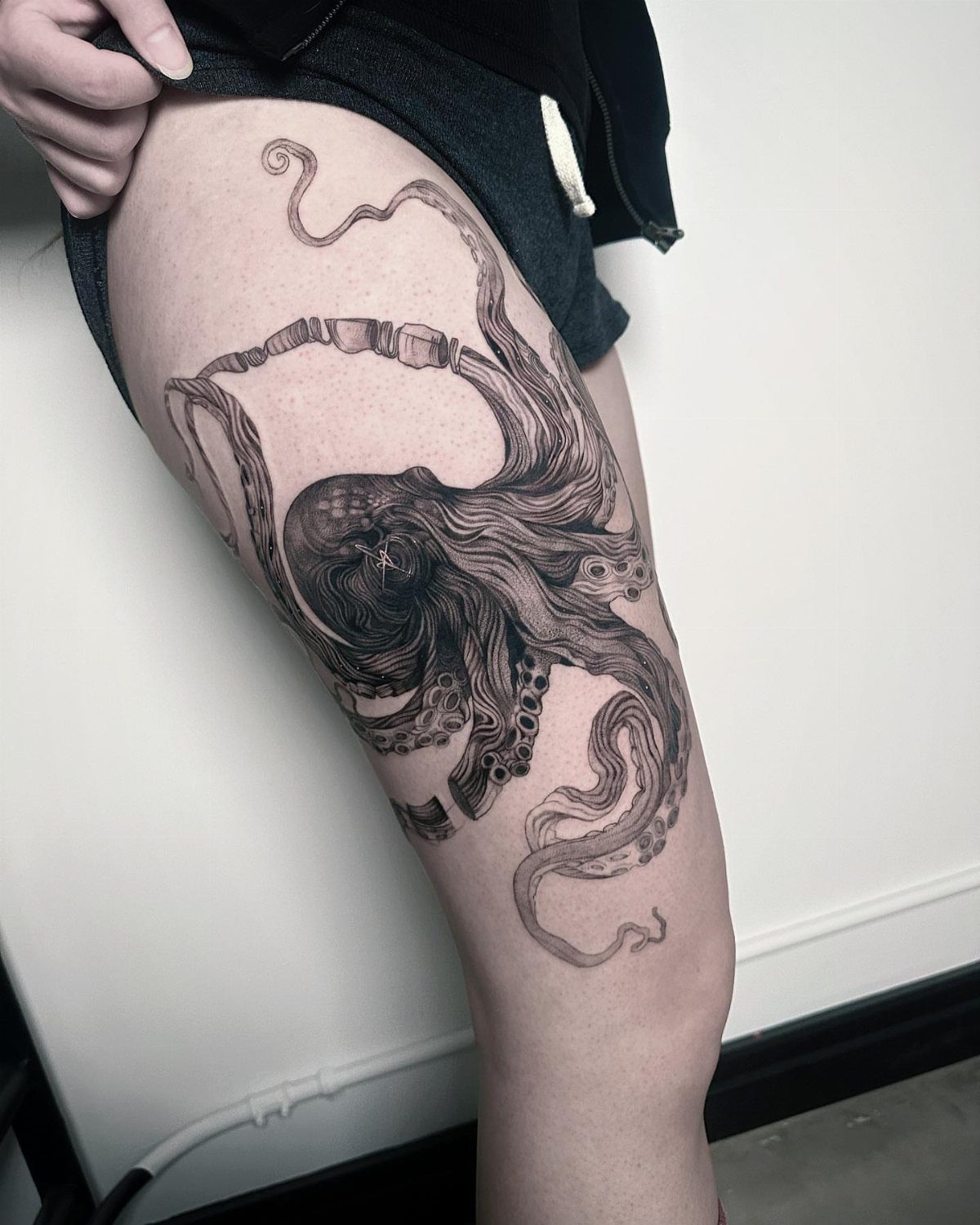 Octopus tattoo on a woman's thigh with detailed black and grey ink tentacles.