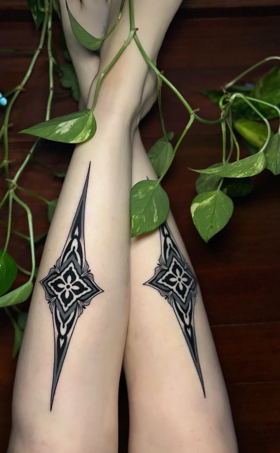 Symmetrical black ornamental tattoos on thighs with green leaves draped over legs