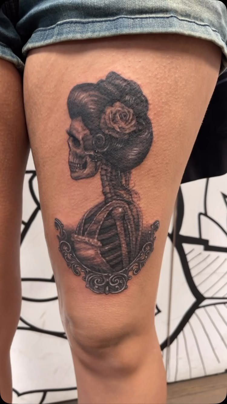 Skeletal woman tattoo with a rose in her hair on a side thigh.