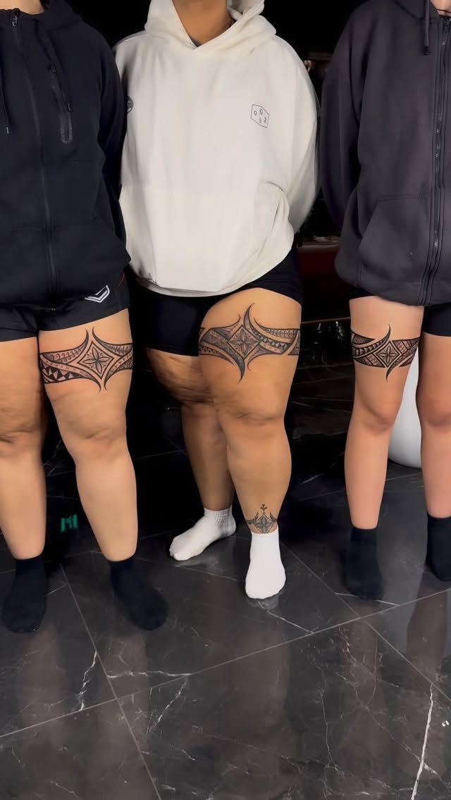 Three women with matching ornamental black ink band tattoos on their upper thighs.