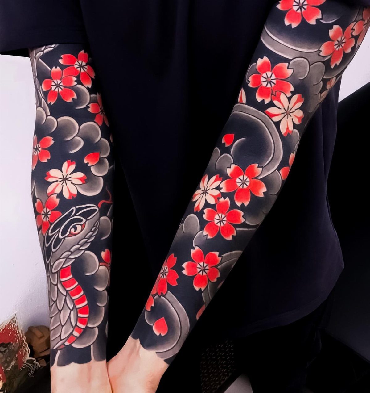 Traditional Japanese tattoo sleeves with red cherry blossoms and a snake on arms.