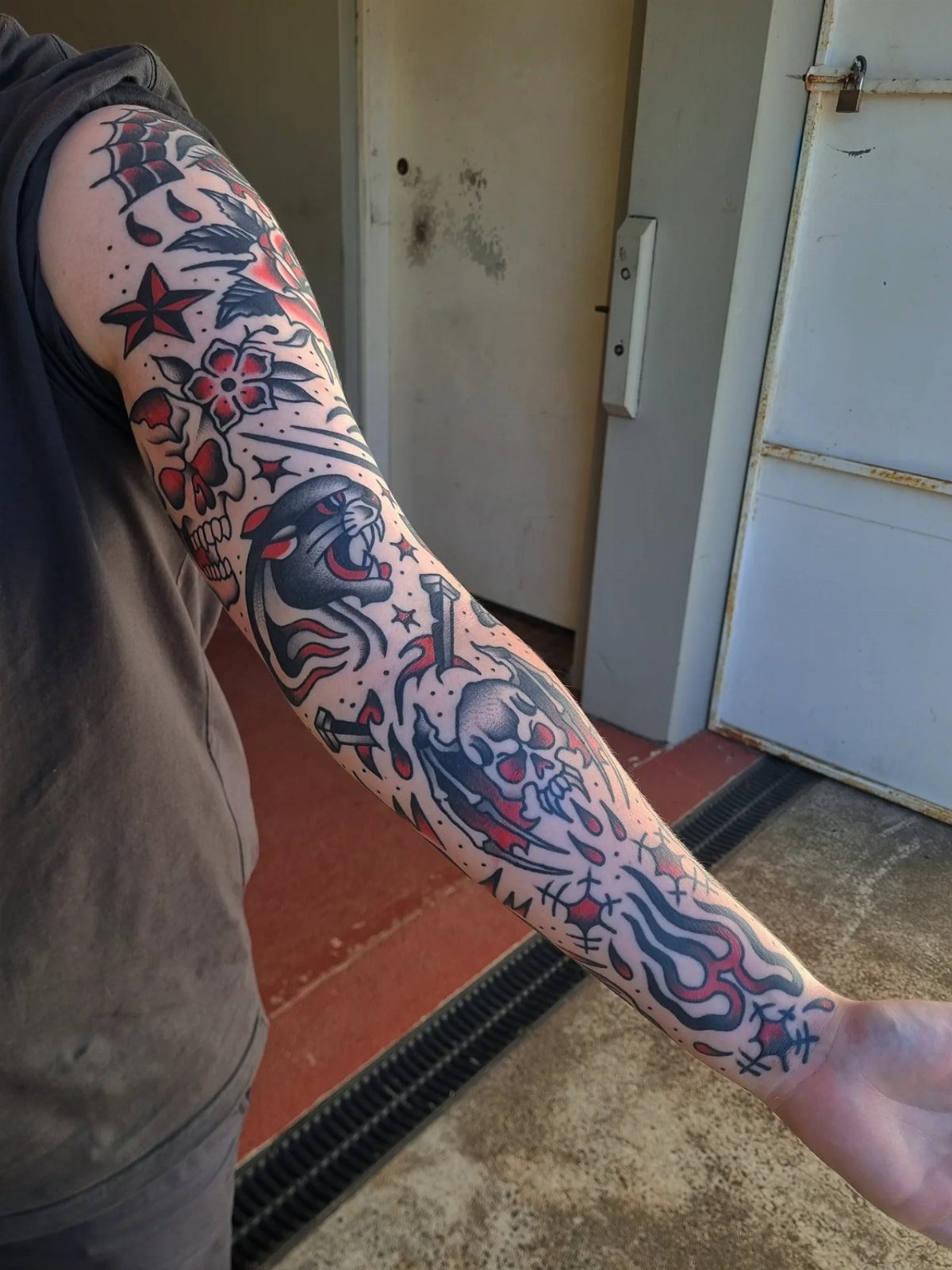 Traditional tattoo sleeve on an arm featuring a panther, skull, and red flowers.