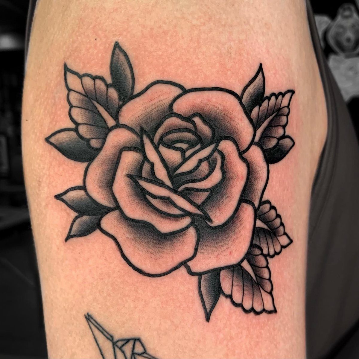 Traditional rose tattoo with bold black outlines and grey shading on skin