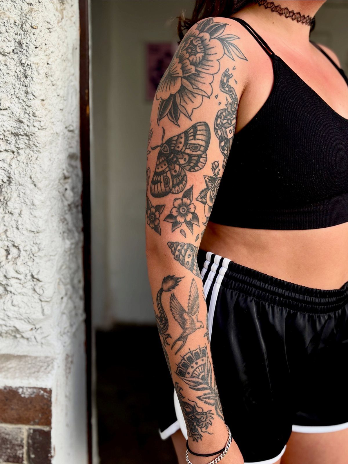 Woman's arm with a full sleeve of traditional black ink floral and animal tattoos