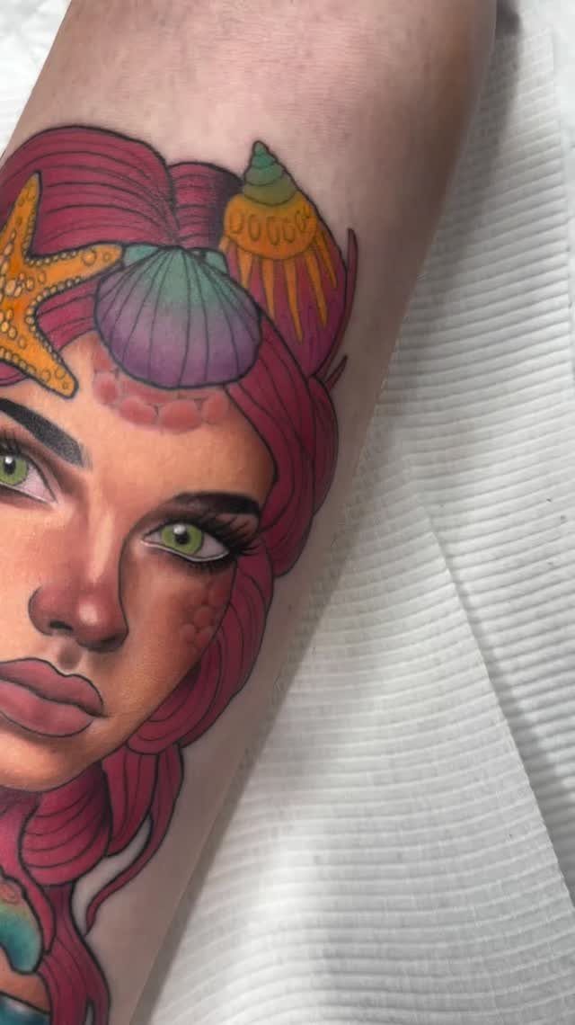 Mermaid tattoo with pink hair and seashells on a person's arm.