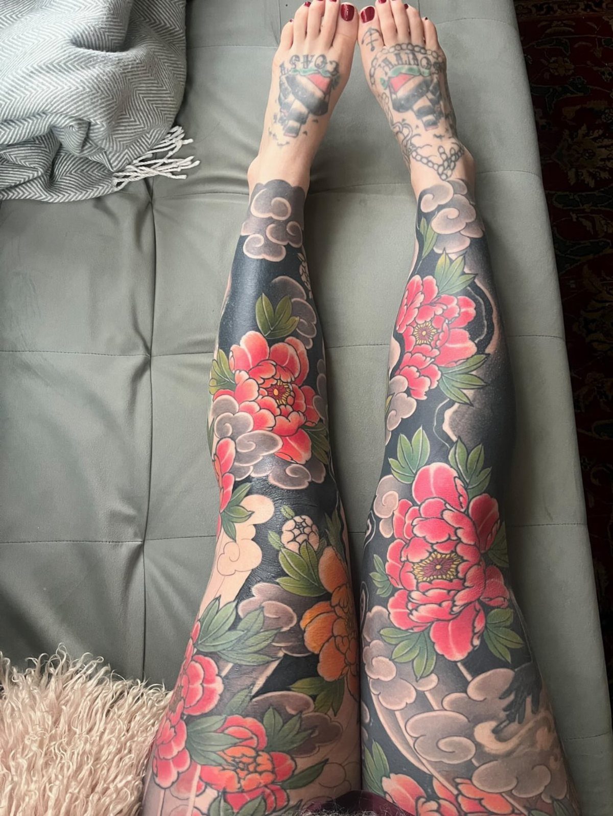 Legs and feet covered in traditional red peony and grey cloud tattoos.
