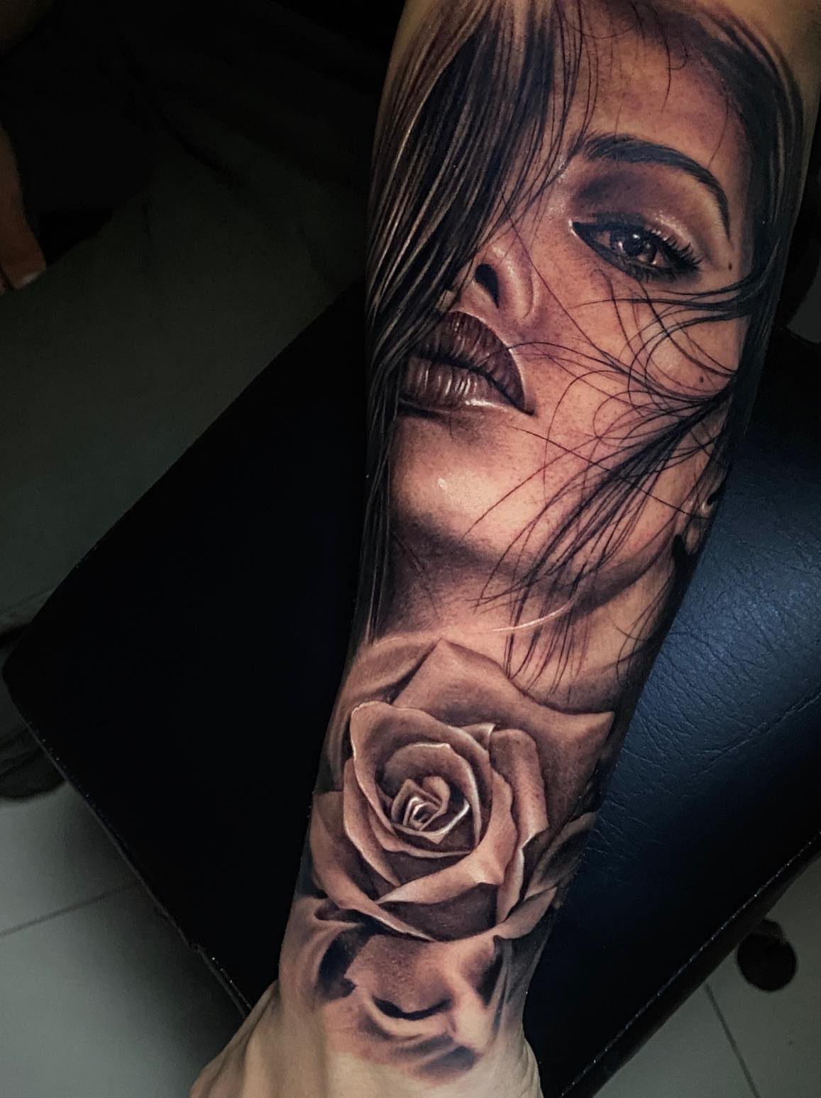 Woman's face and a rose flower in a realistic black and grey tattoo.