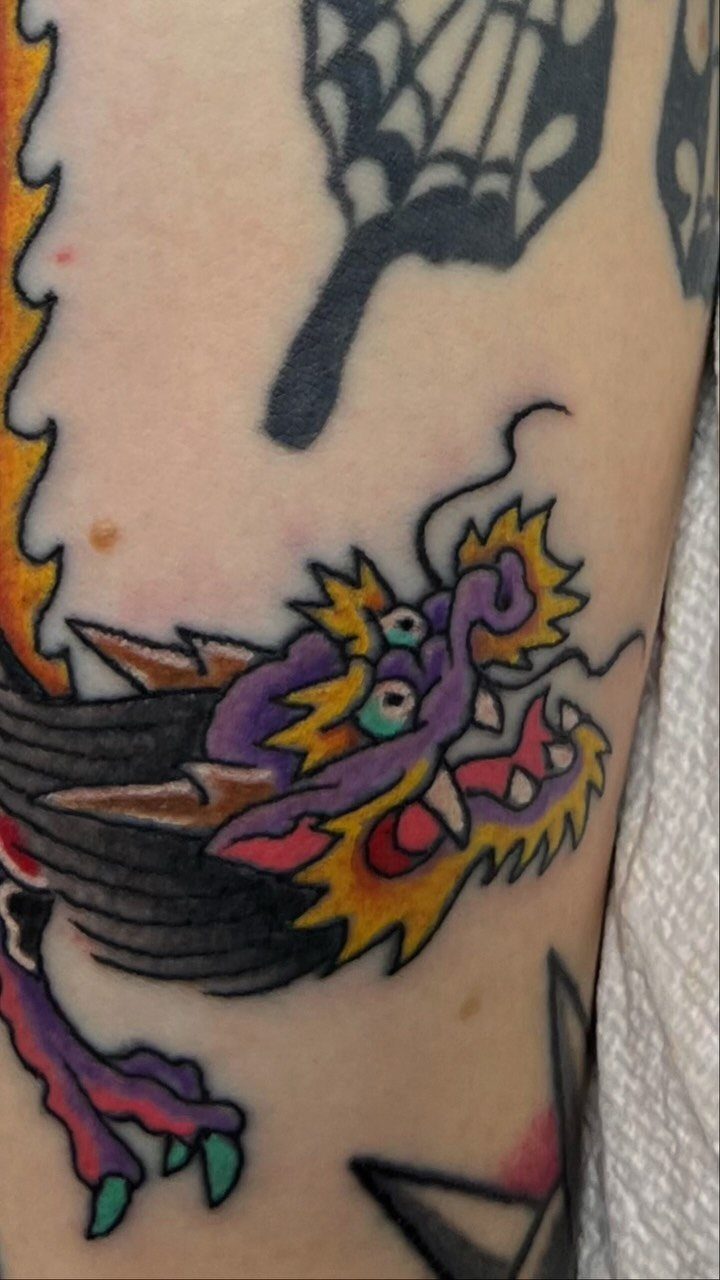 Traditional style dragon tattoo with purple and yellow colors on a person's skin.