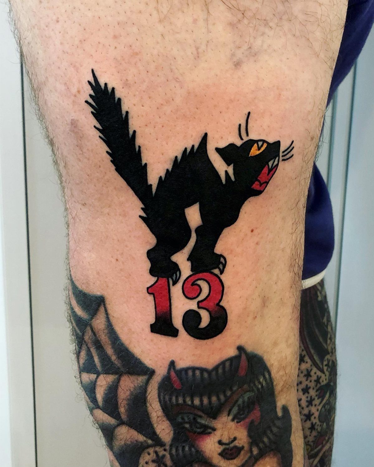 Black cat tattoo standing on a red number 13 on a man's leg.