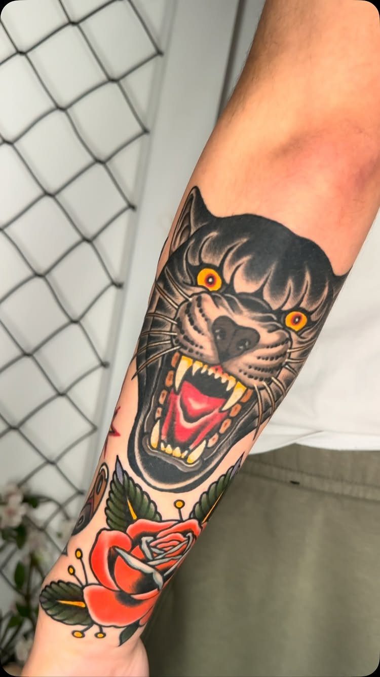Black panther head tattoo with yellow eyes and a red rose on forearm