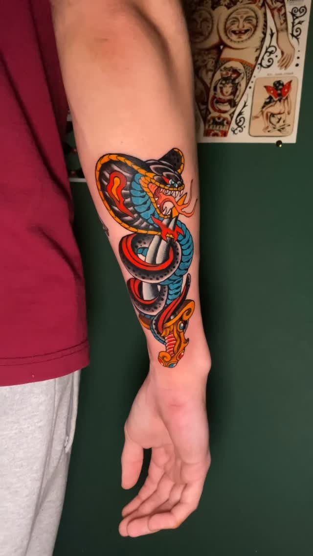 Traditional tattoo of a blue cobra snake wrapped around a silver dagger on forearm.