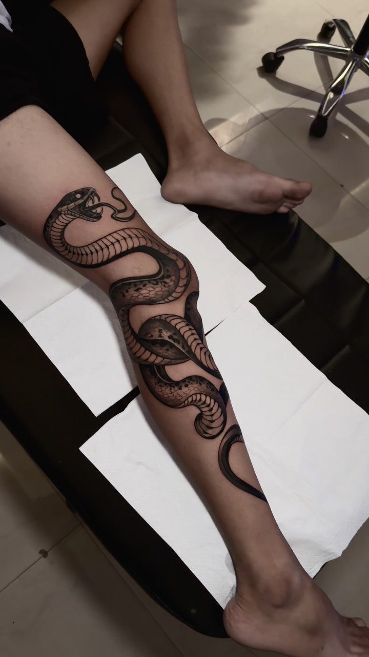 Traditional snake tattoo wrapping around a person's lower leg on a tattoo table.