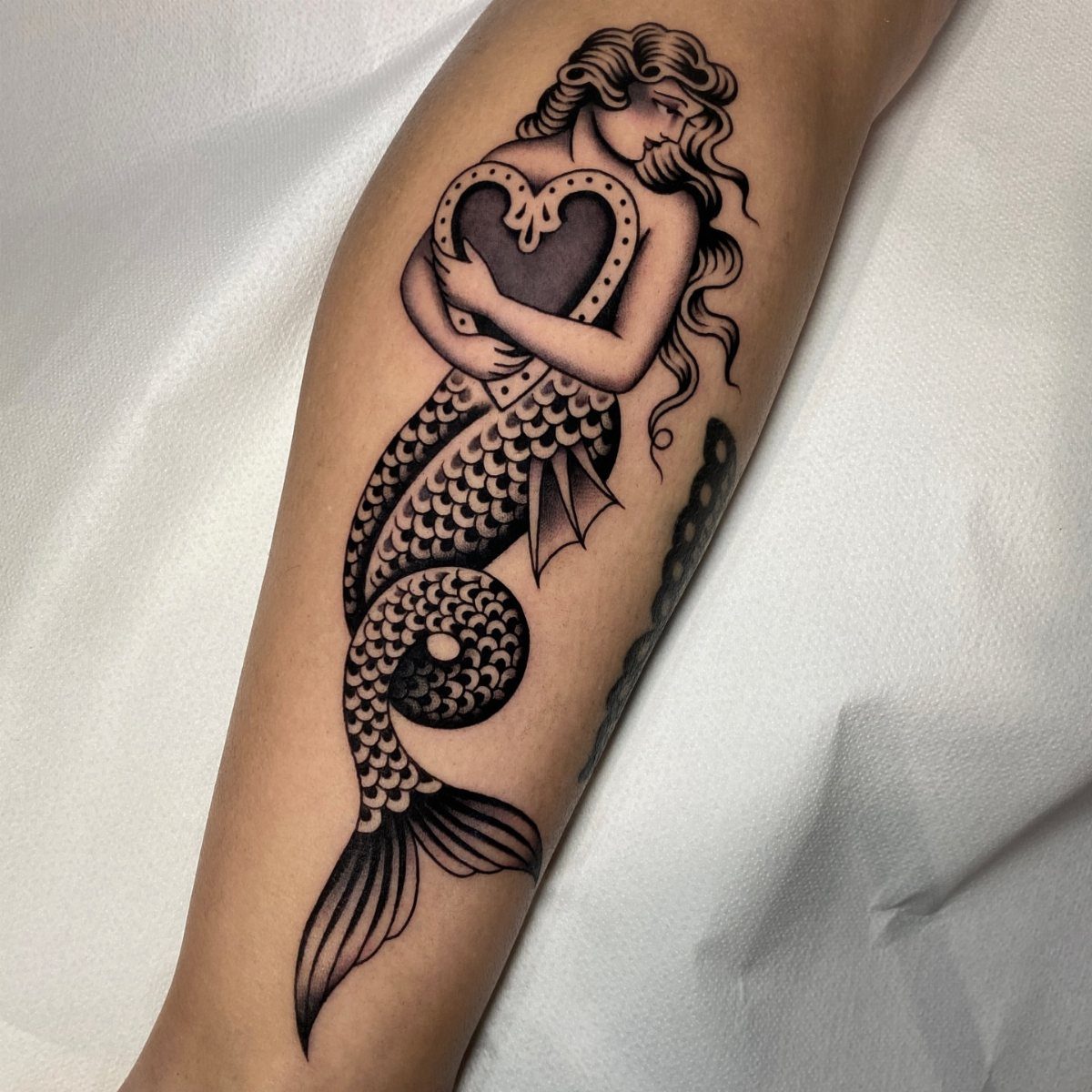 Traditional mermaid tattoo in black and grey ink on a person's forearm.