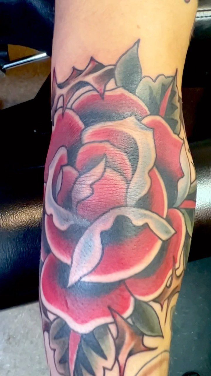 Traditional red rose tattoo with green leaves on a person's arm.