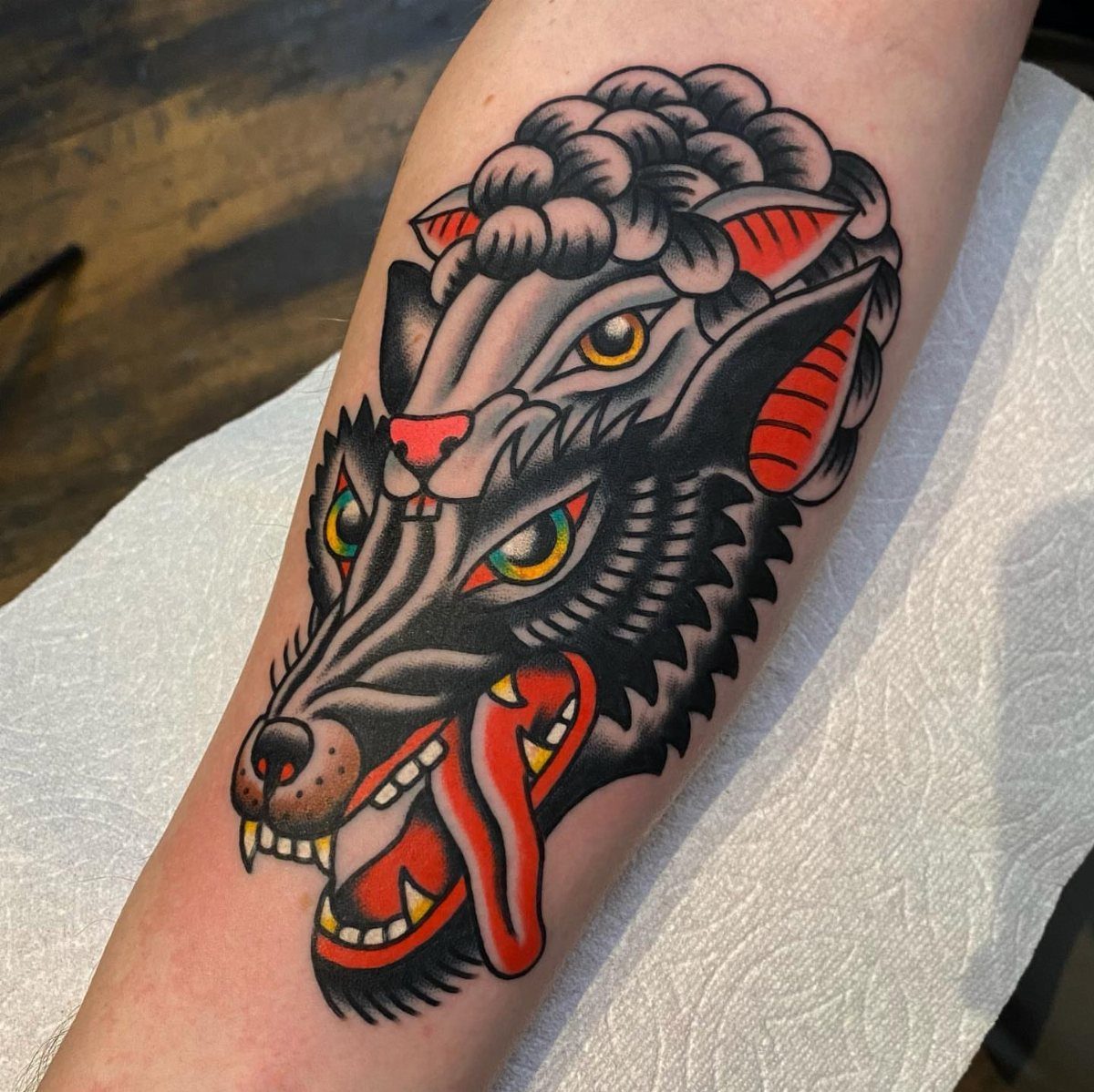 Traditional wolf head tattoo with a sheep's head behind it on a forearm
