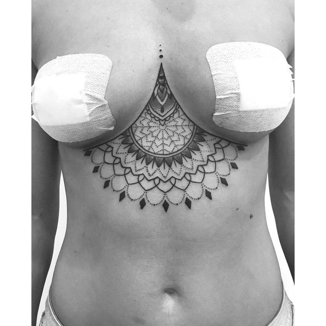 Intricate mandala tattoo on a woman's torso located beneath the breasts.