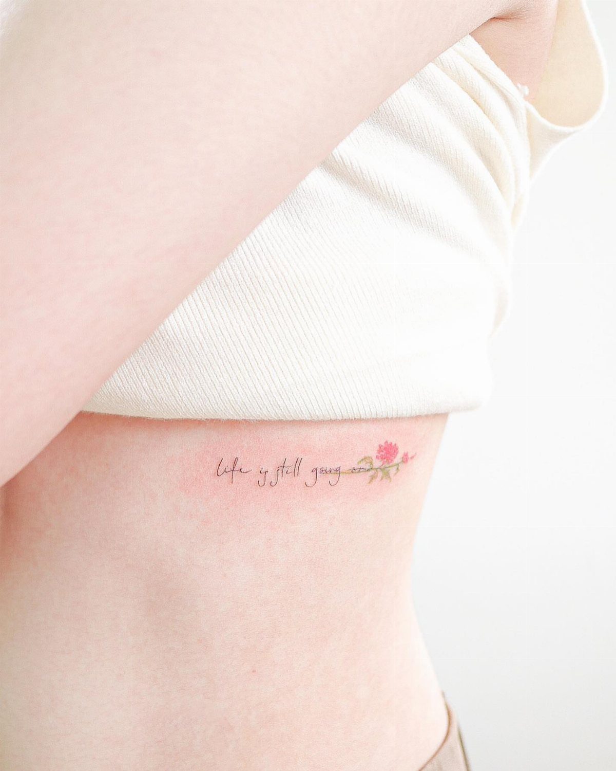 Script tattoo with a small red flower on a woman's ribcage underboob area.