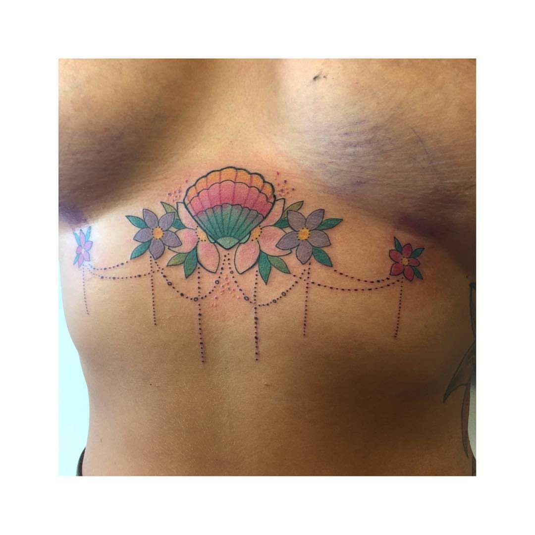 Colorful seashell and flower tattoo located on the underboob area of a woman.
