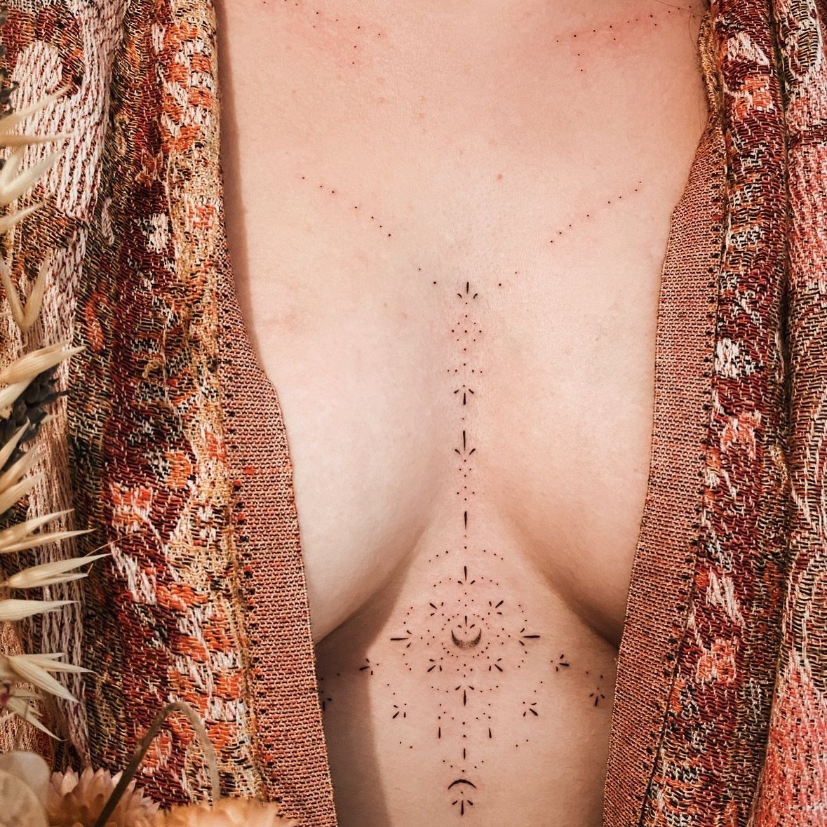 Fine-line underboob tattoo with a crescent moon and dots on a woman's chest.