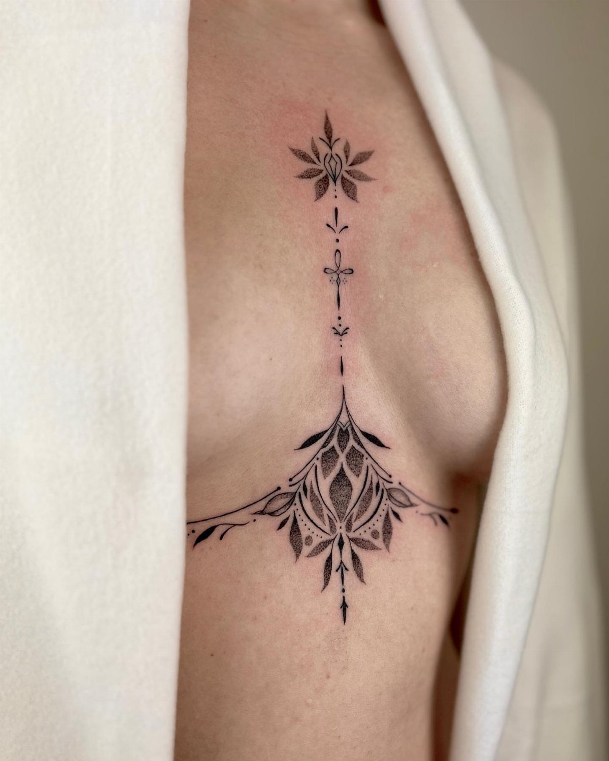 Symmetrical black ink ornamental tattoo on a woman's sternum and underboob area.