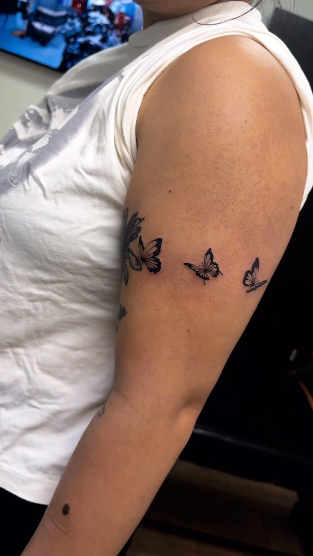 Three small black butterfly tattoos in a row on a person's upper arm.