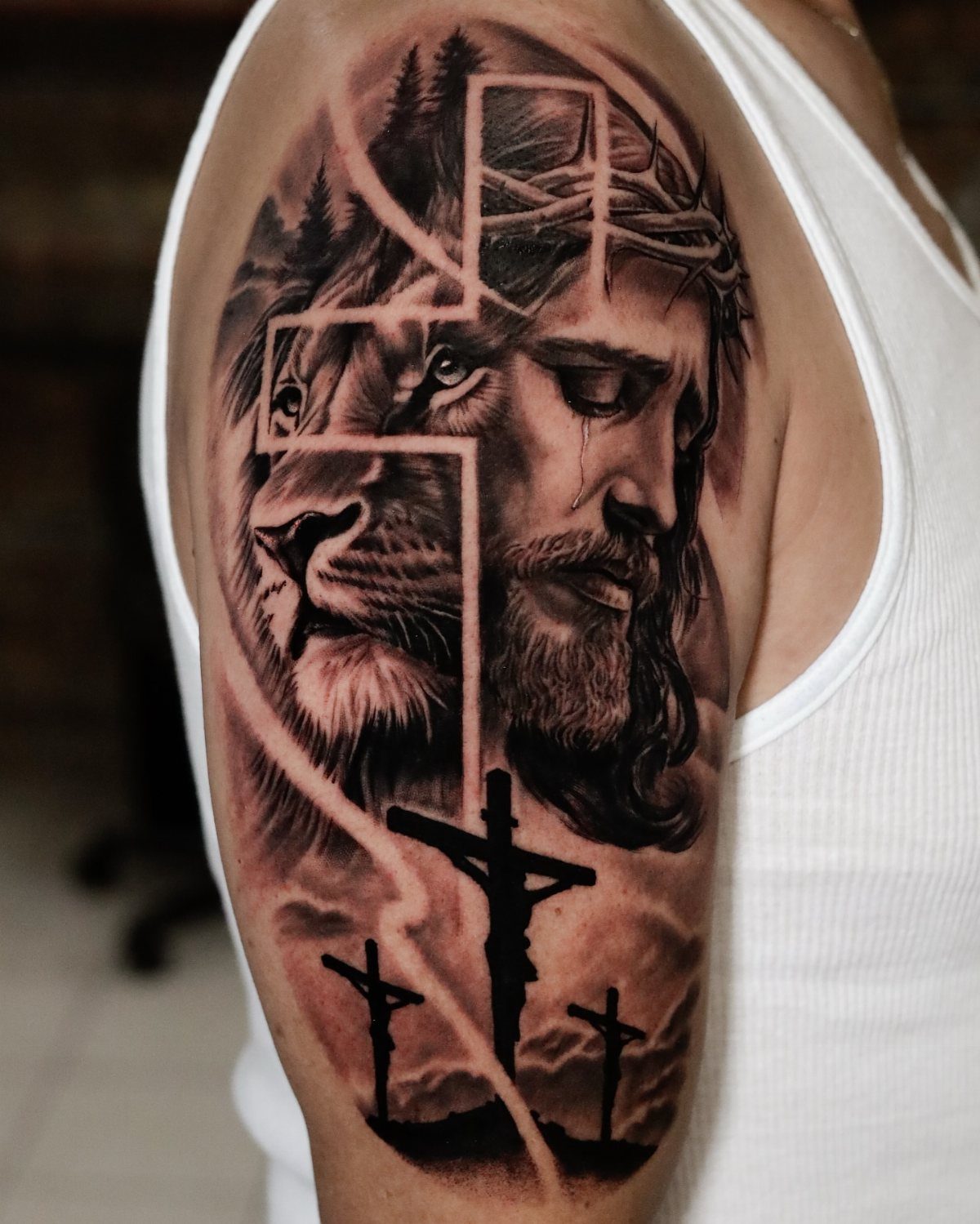 Cross tattoo on upper arm featuring Jesus, a lion, and three crosses.