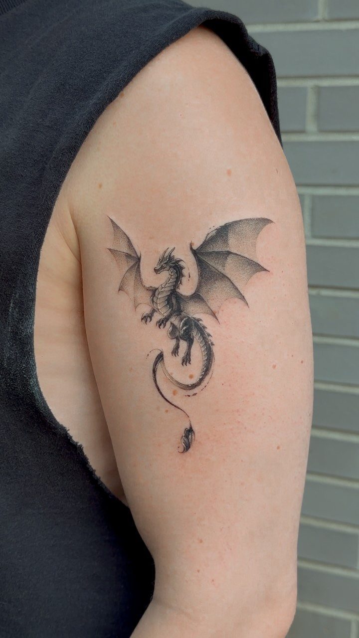 Dragon tattoo with open wings on a person's upper arm against brick wall