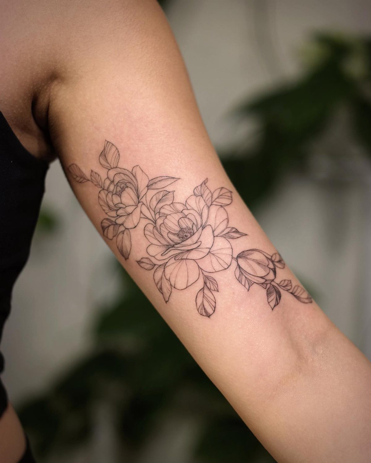 Rose flower tattoo in black line art on a person's upper arm.