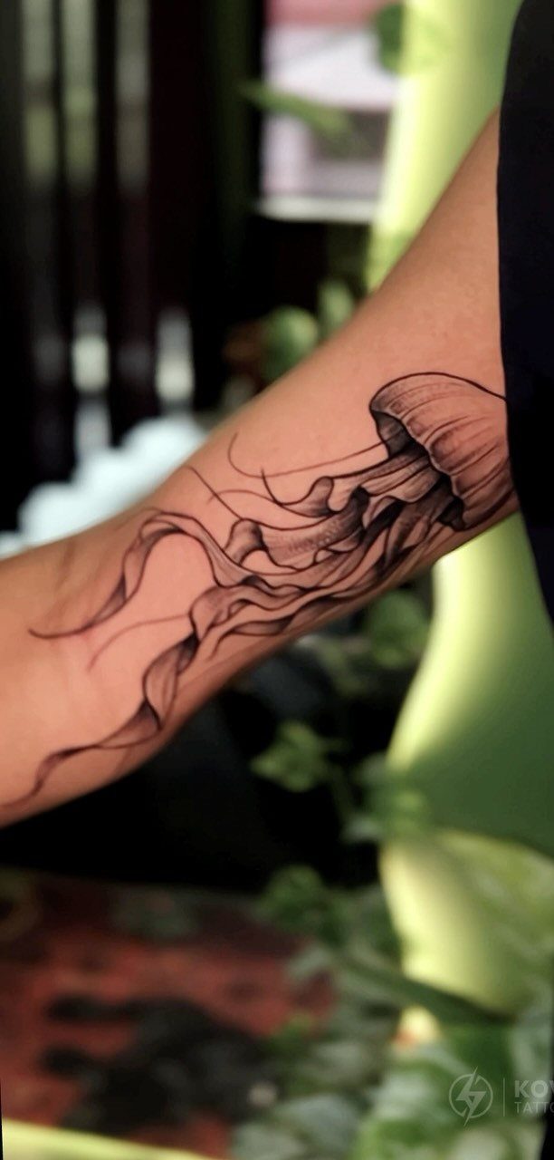 Jellyfish tattoo with detailed tentacles on a person's upper arm in black ink.