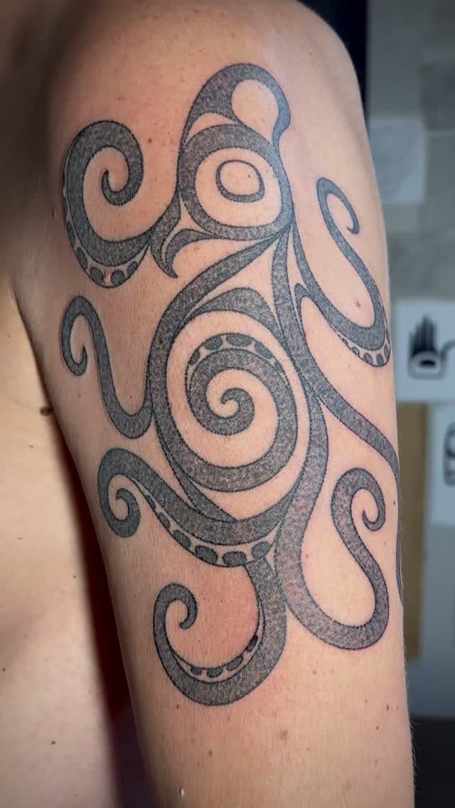 Stylized octopus tattoo with swirling tentacles on a person's upper arm.