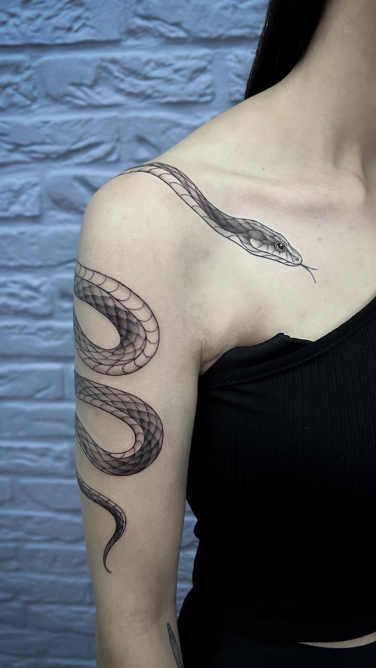 Snake tattoo wrapping around a person's upper arm and shoulder against brick wall