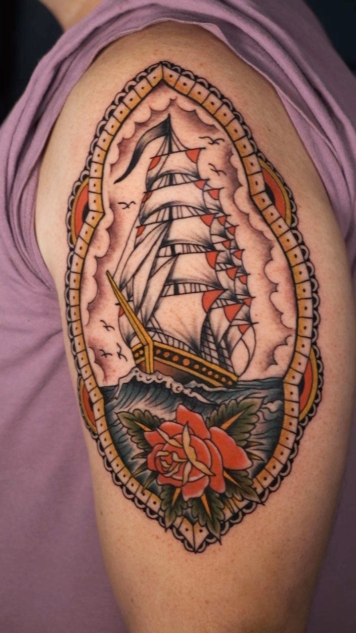 Traditional upper arm tattoo of a sailing ship and red rose in an ornate frame