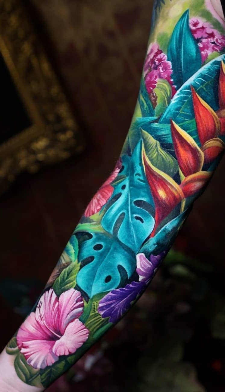 Colorful tropical tattoo on an arm with hibiscus and bird-of-paradise flowers