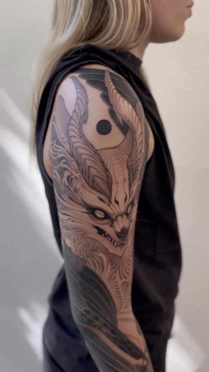 Detailed black and grey horned creature tattoo on a woman's upper arm