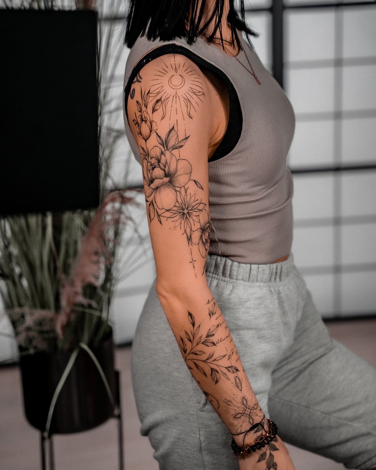 Woman's arm with black ink tattoos featuring floral patterns and geometric sun lines.