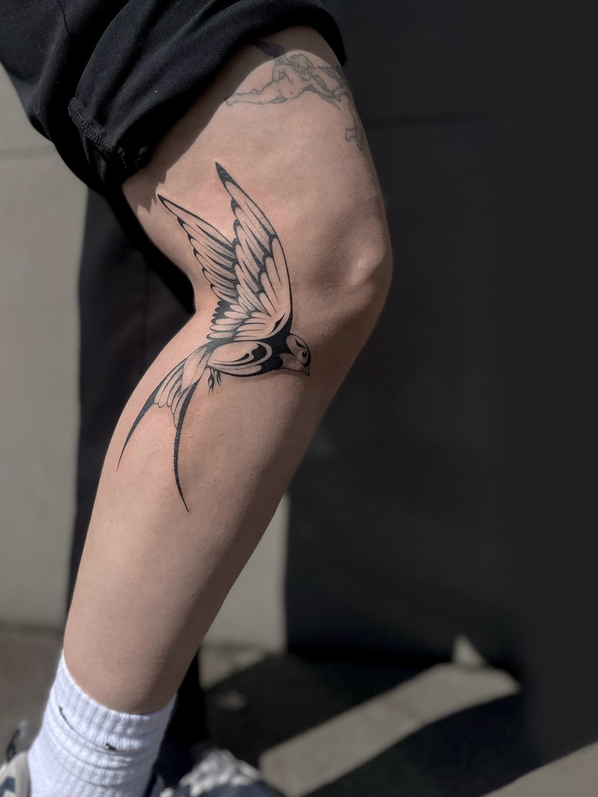 Swallow bird tattoo on a person's lower thigh and knee area.