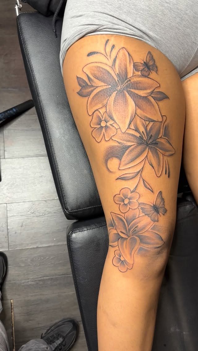 Butterfly and lily tattoos on a person's upper leg in black and grey ink.