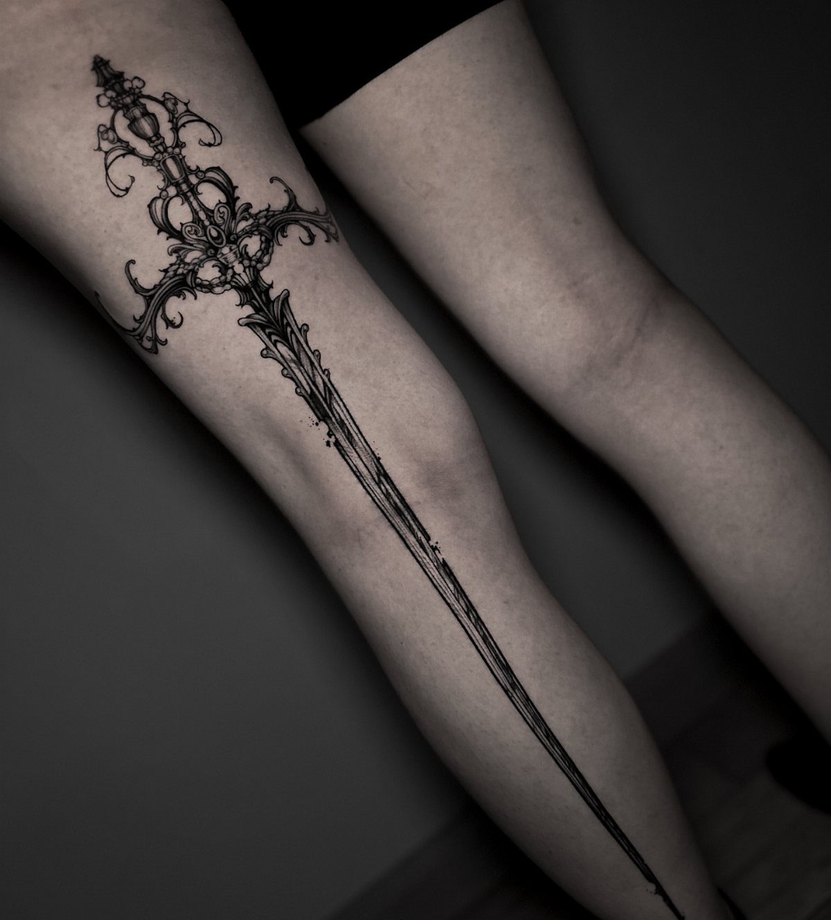 Ornate fantasy sword tattoo extending from the thigh down the leg in black ink.