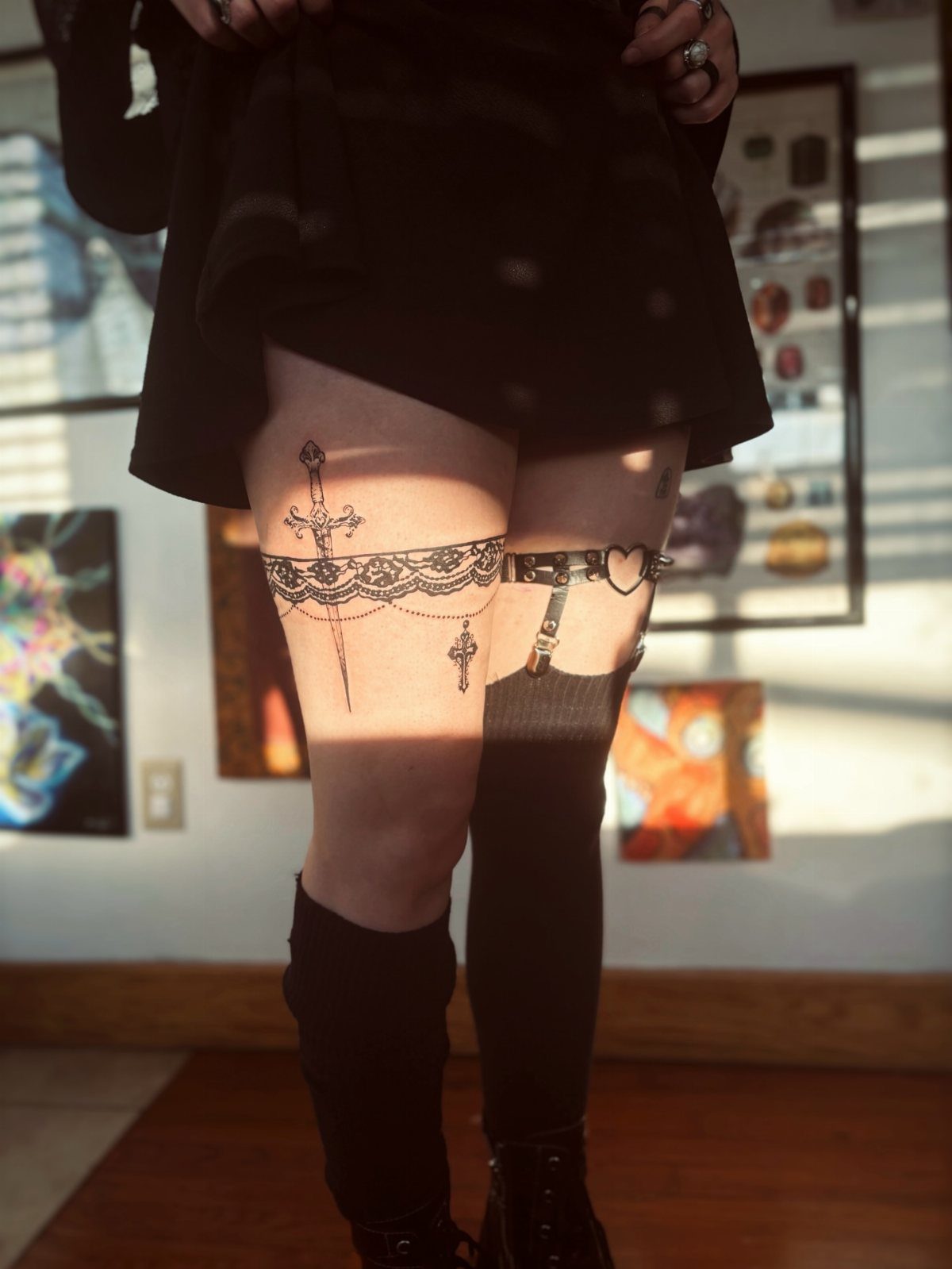 Lace garter thigh tattoo with a sword and charms on a person's leg.