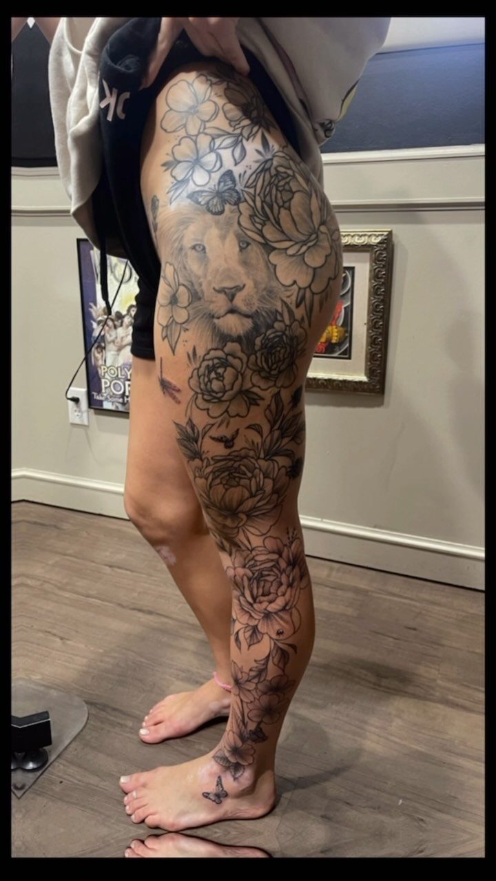 Large black and grey tattoo of a lion and roses on a leg
