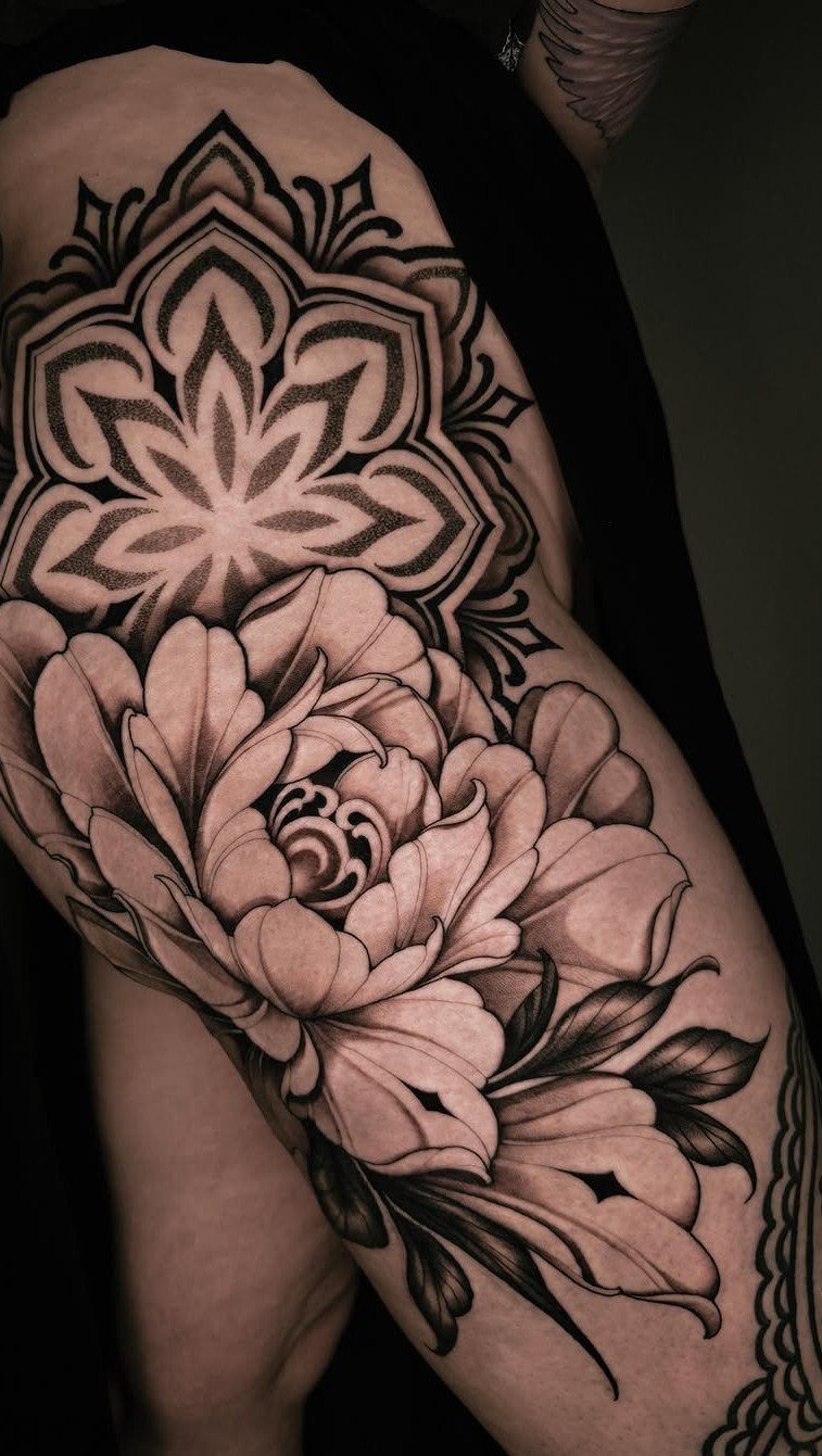 Mandala and peony flower tattoo on a person's upper leg in black and grey.