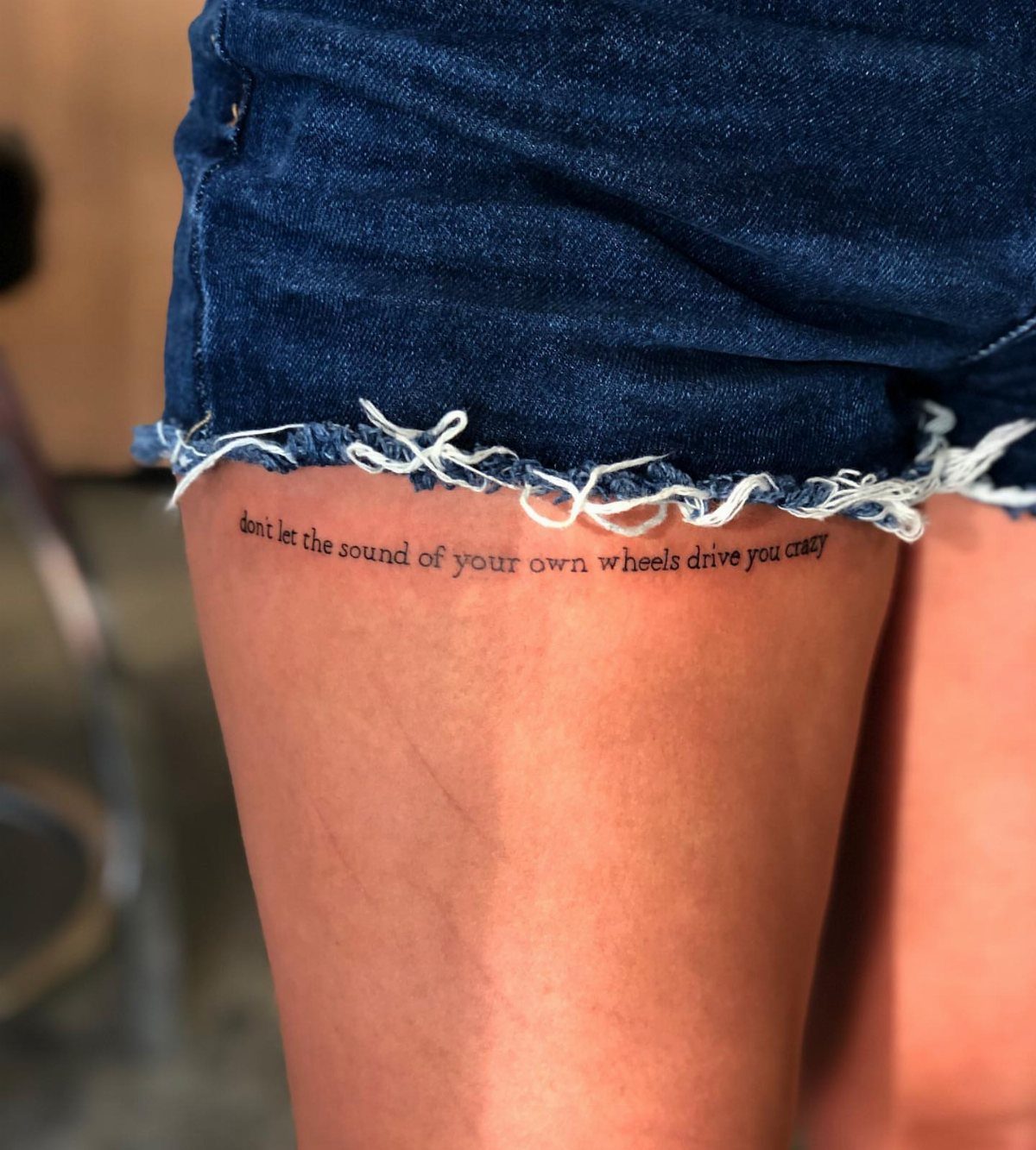 Cursive quote tattoo on a person's upper leg wearing blue denim shorts